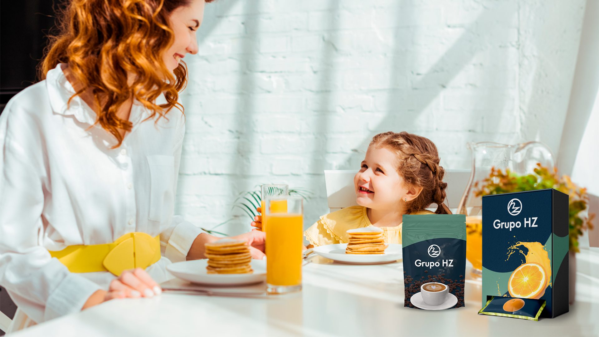 En la imagen se muestra una señora y su hija desayunando y hay dos envoltorios de grupohz de cafe y naranja.